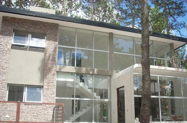 Edificio moderno de dos plantas con grandes ventanales y exterior de ladrillo y estuco entre árboles.