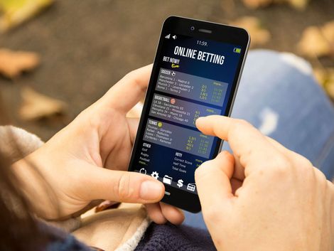 A person is holding a cell phone with a betting app on it.