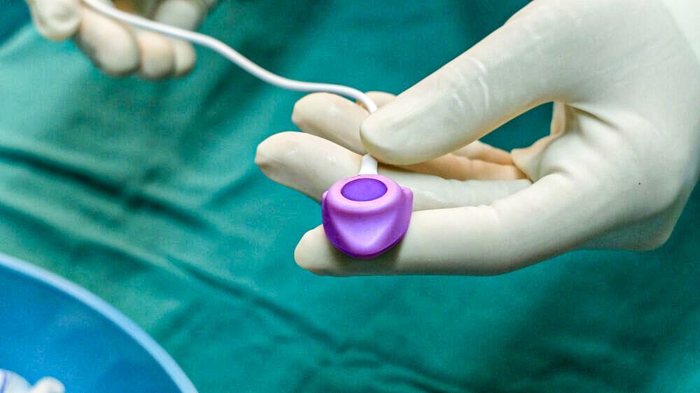A close up of a person wearing medical gloves holding a Bard PowerPort in their hand.