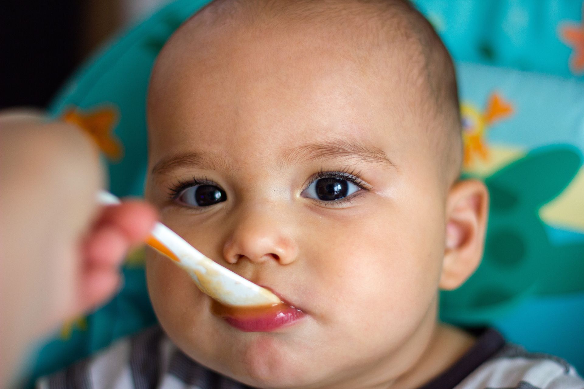 A baby is being fed with a spoon in a high chair.