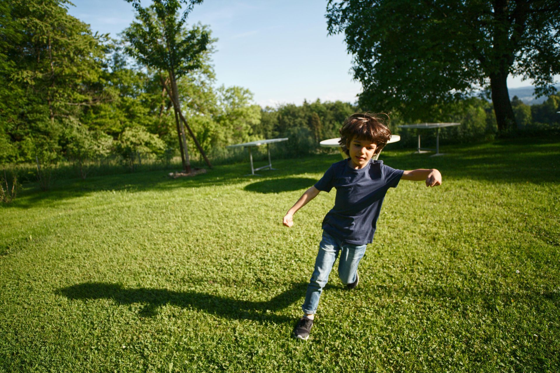 Boy in a blue shirt and jeans running on a green lawn in bright sunlight.