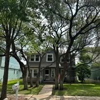 Two-story gray house with large trees and a front walkway in a residential neighborhood