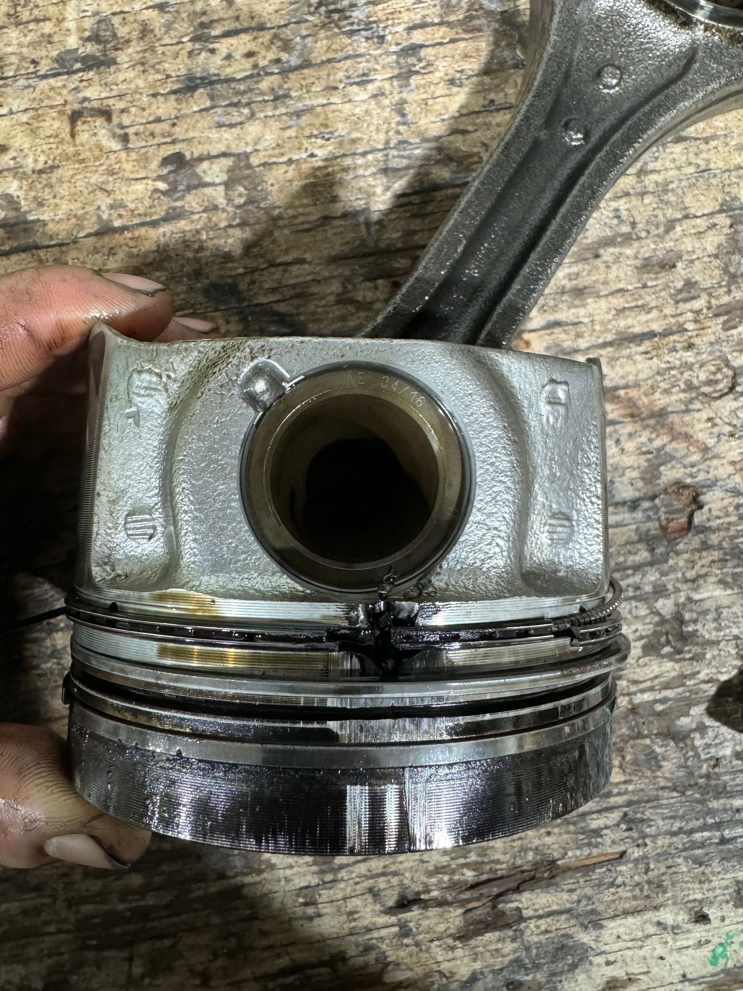 Piston with broken rings and connecting rod, likely from a vehicle engine. Metal on a wood surface. | Ace-High Diesel
