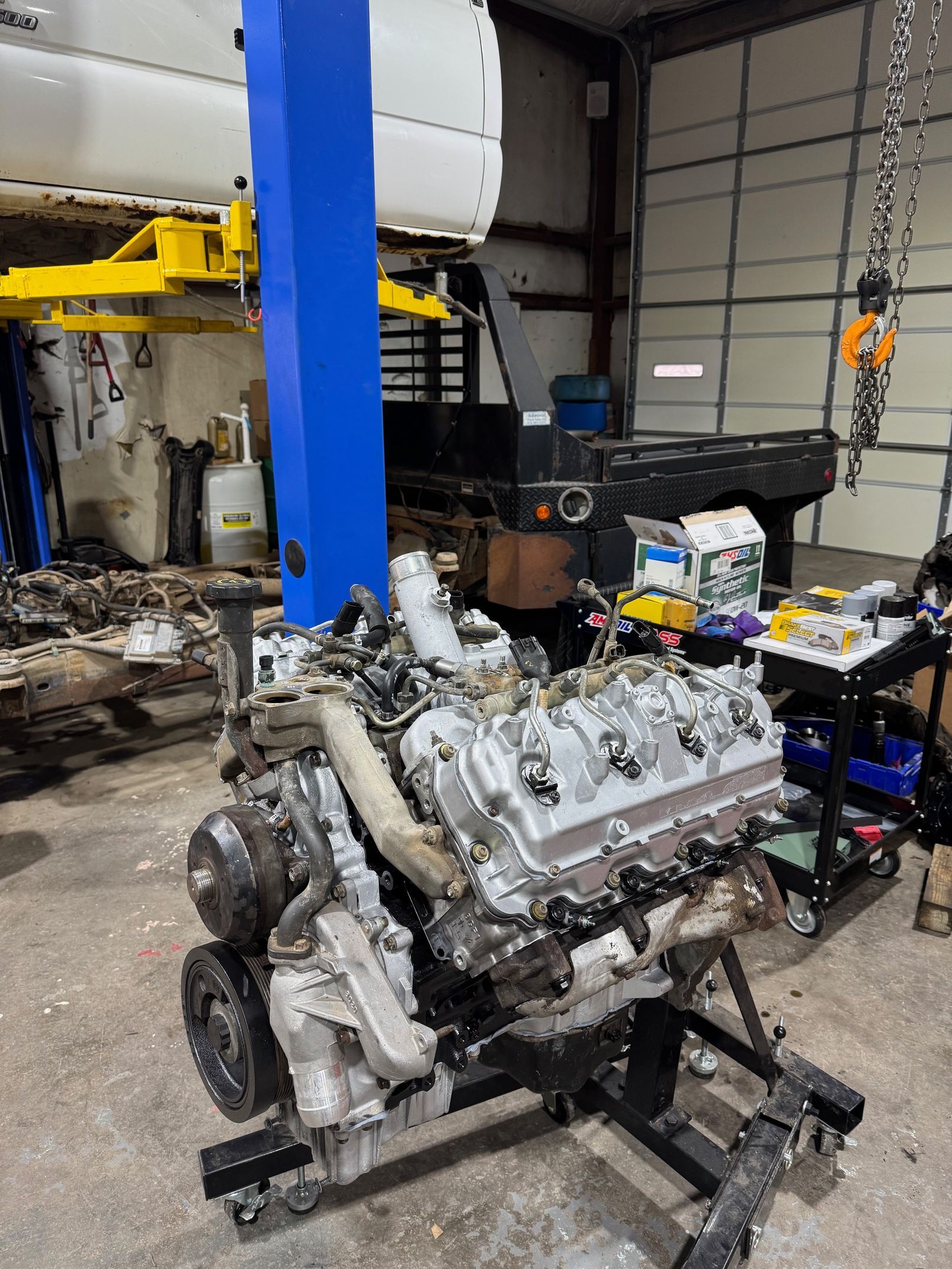 Engine on a stand in a garage. Overhead lift and tool cart are visible. | Ace-High Diesel