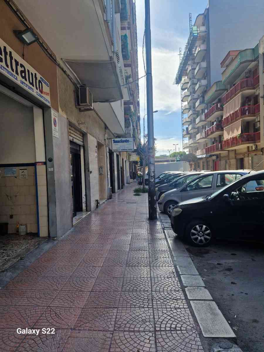 Stretto marciapiede cittadino accanto ad auto parcheggiate e palazzi residenziali sotto un cielo luminoso