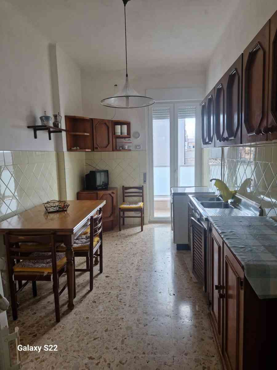 Cucina stretta con mobili in legno, paraschizzi piastrellato, tavolo da pranzo e porta scorrevole in vetro in fondo.