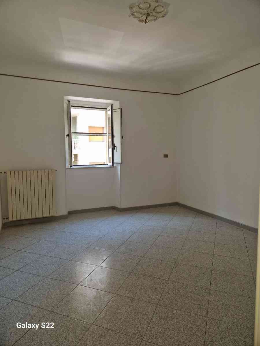 Stanza bianca vuota con pavimento piastrellato, piccola finestra e termosifone vicino alla parete.