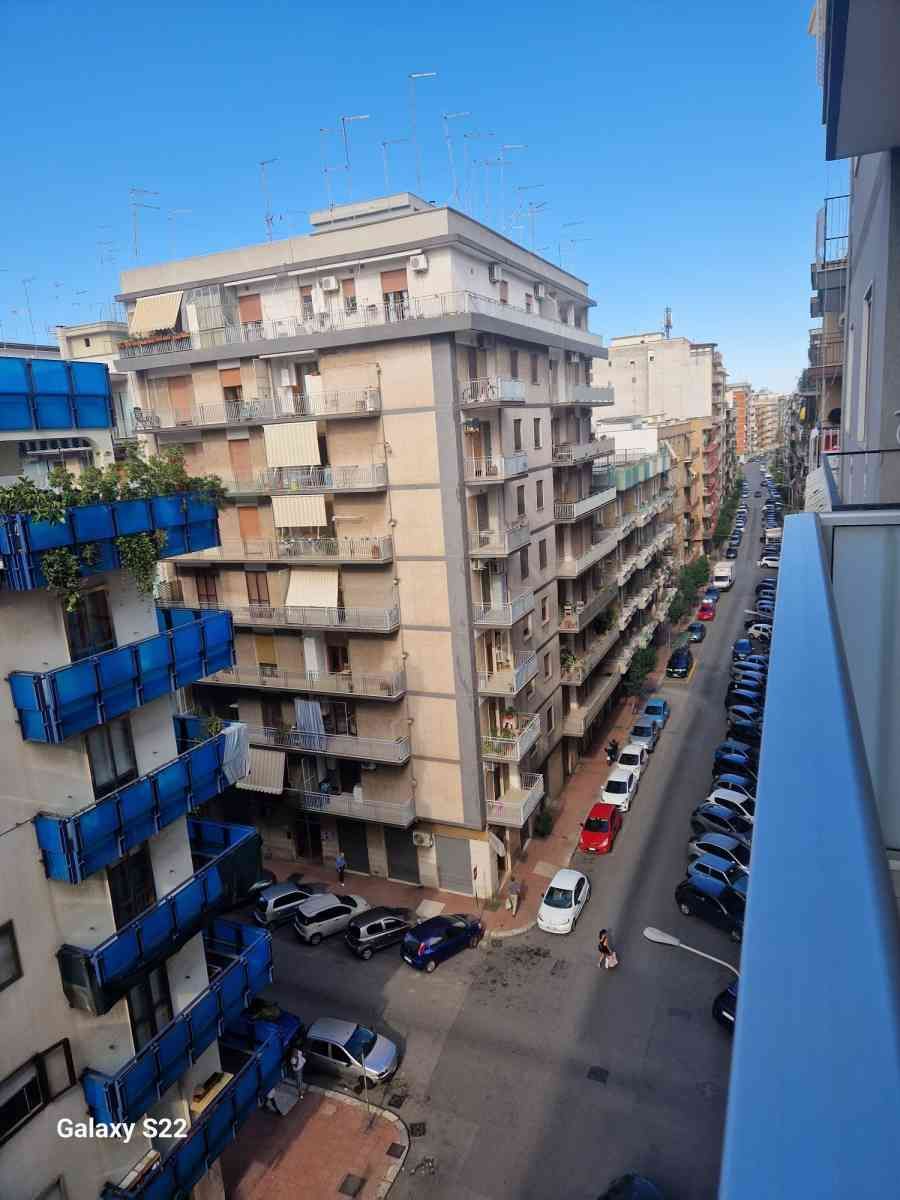 Veduta urbana di una strada stretta con palazzi residenziali, impalcature blu e auto parcheggiate.
