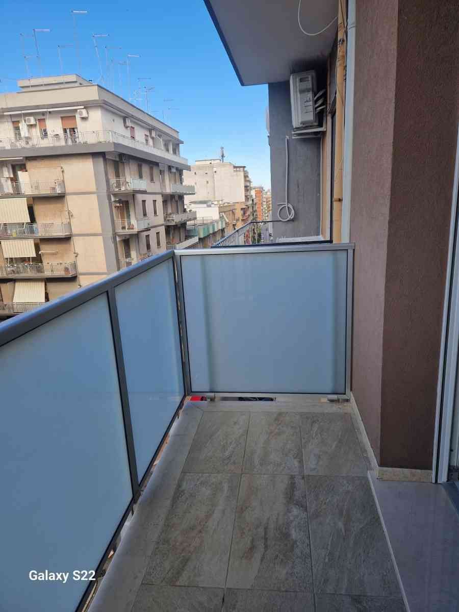Stretto balcone di appartamento con ringhiera in vetro satinato e vista sugli edifici della città.