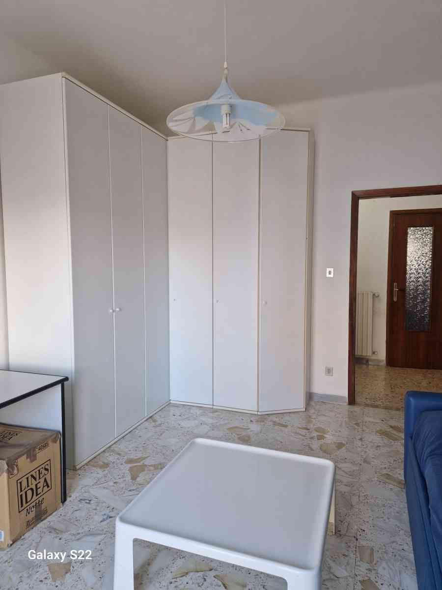 Piccola camera da letto con armadi bianchi, pavimento piastrellato e lampada a soffitto.