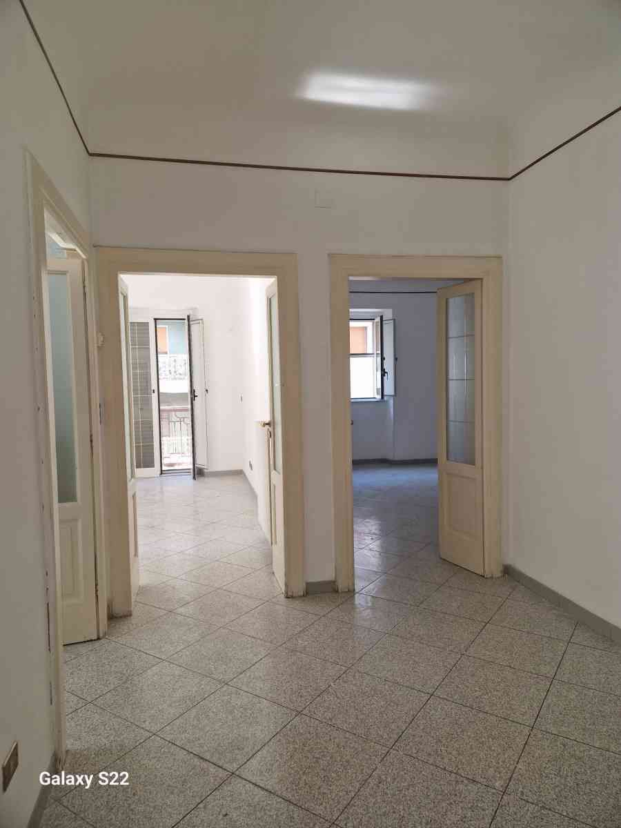 Corridoio bianco vuoto con pavimento piastrellato e porte aperte verso le stanze adiacenti.