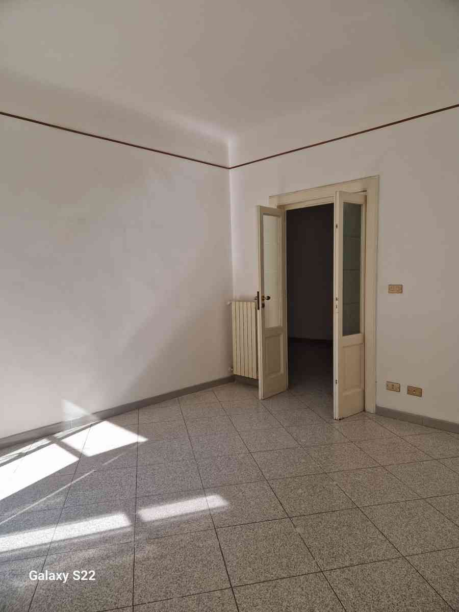 Stanza vuota piastrellata con pareti bianche, porta aperta e luce del sole che filtra sul pavimento.