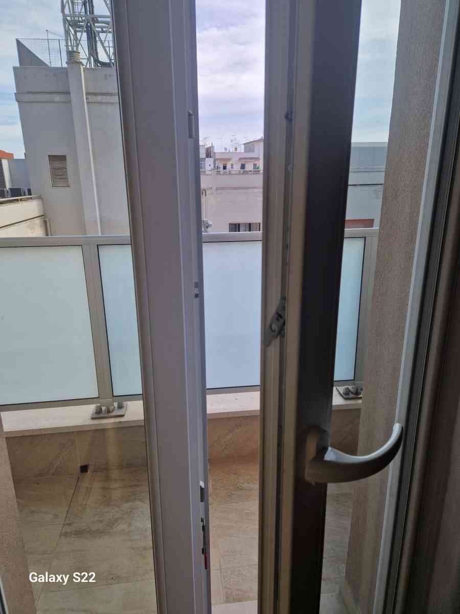 Vista dal balcone attraverso una porta a vetri sugli edifici circostanti e sul lungomare.