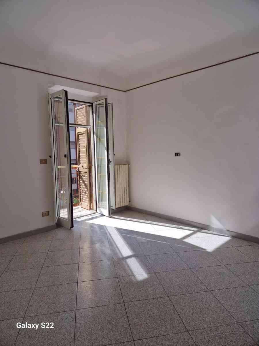 Stanza vuota con pareti bianche, pavimento piastrellato e una porta aperta che lascia entrare la luce del sole.