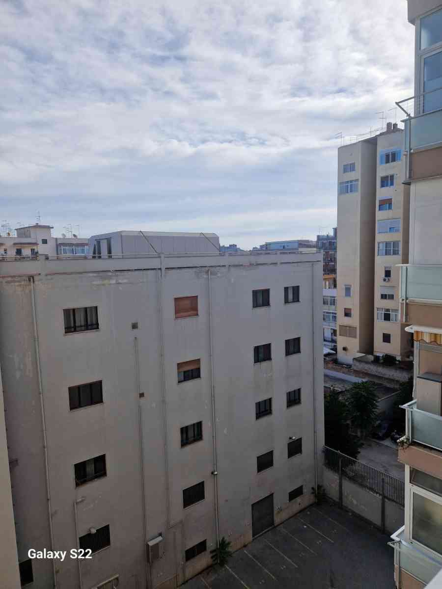 Veduta della città con palazzi residenziali bianchi sotto un cielo nuvoloso, e un alto edificio beige sulla destra.
