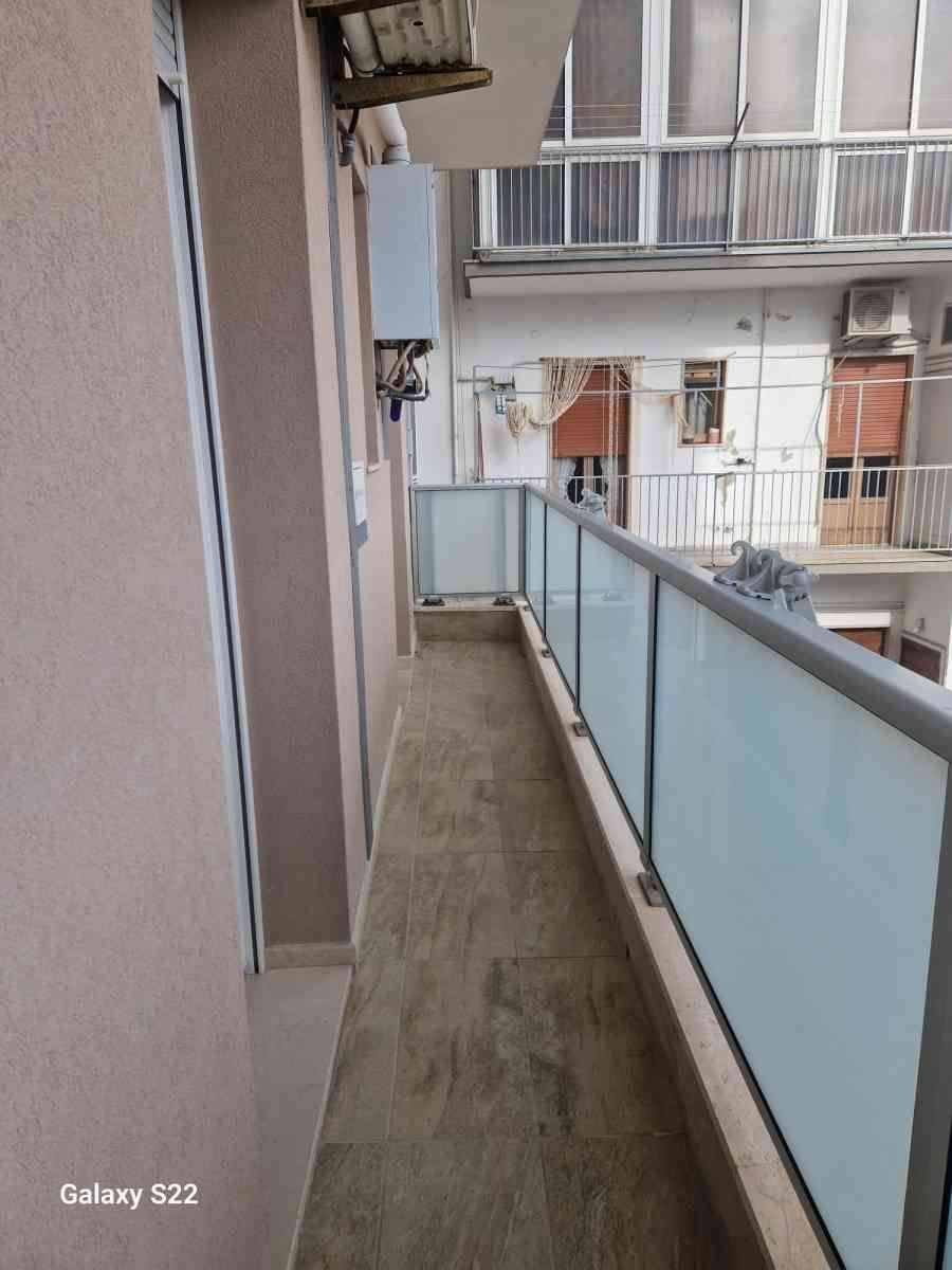 Stretto balcone di un appartamento con ringhiera in vetro satinato, affacciato sugli edifici circostanti.