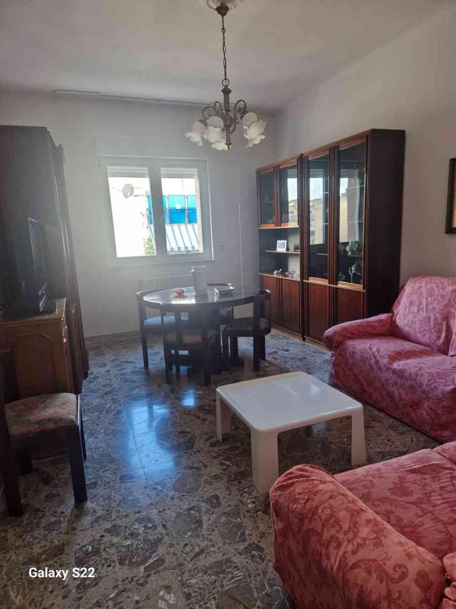 Soggiorno con divani floreali, tavolo da pranzo, vetrina e lampadario vicino a una finestra