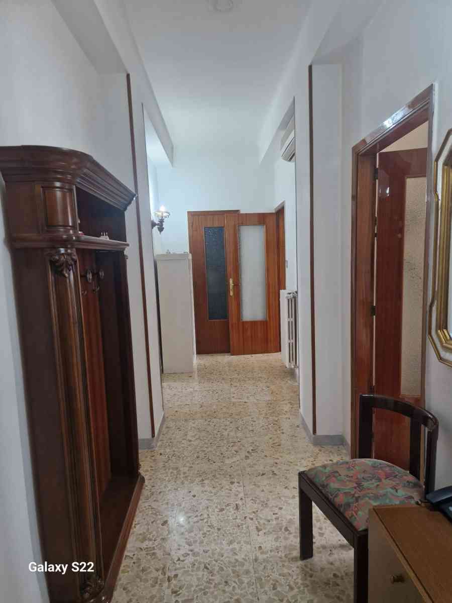 Stretto corridoio con pareti bianche, pavimento in terrazzo, porte in legno e un armadio sulla sinistra.
