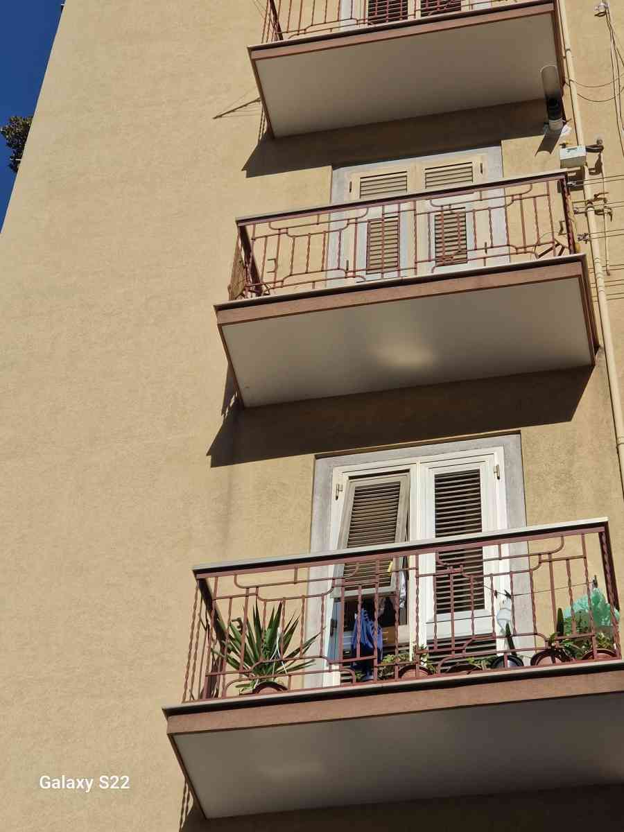 Facciata beige di un condominio con tre piccoli balconi e finestre con persiane bianche.