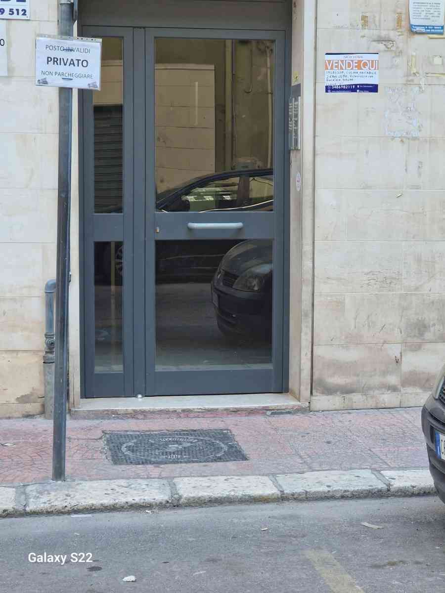 Ingresso del negozio con vetrina, porta grigio-blu e una piccola insegna su una facciata in pietra.
