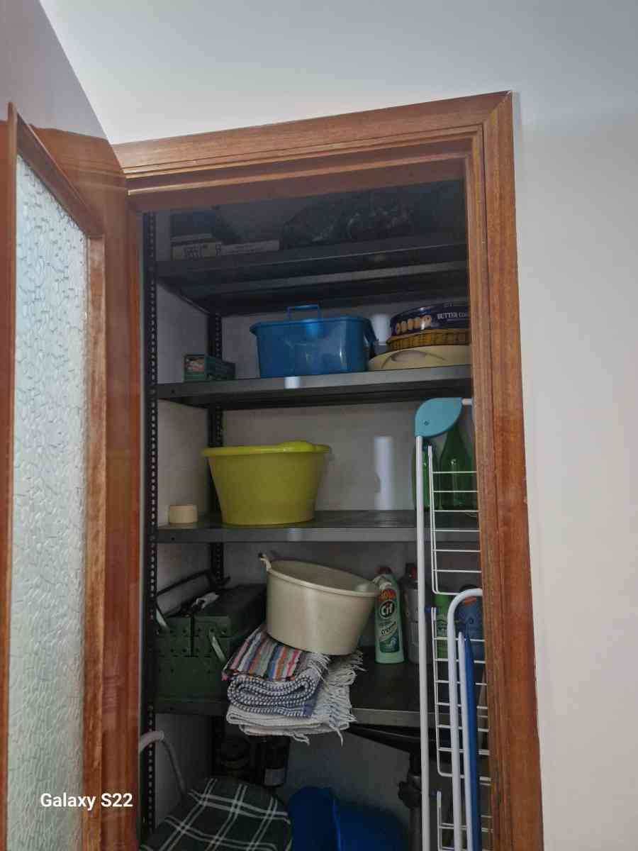 Armadio aperto pieno di scaffali, contenitori, prodotti per la pulizia e articoli per la casa.