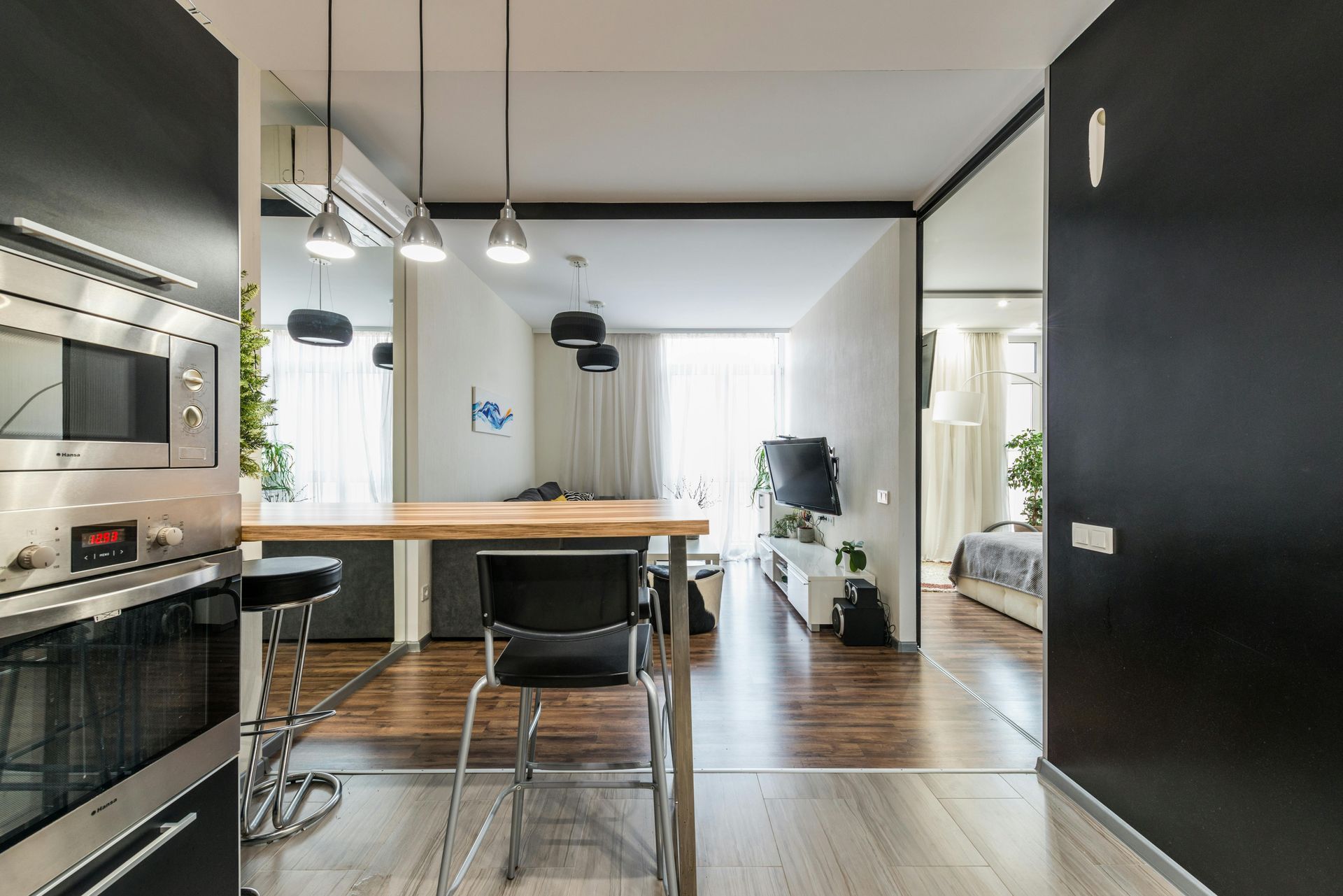 Cucina moderna con isola, lampade a sospensione, mobili neri e vista aperta su una luminosa zona giorno.