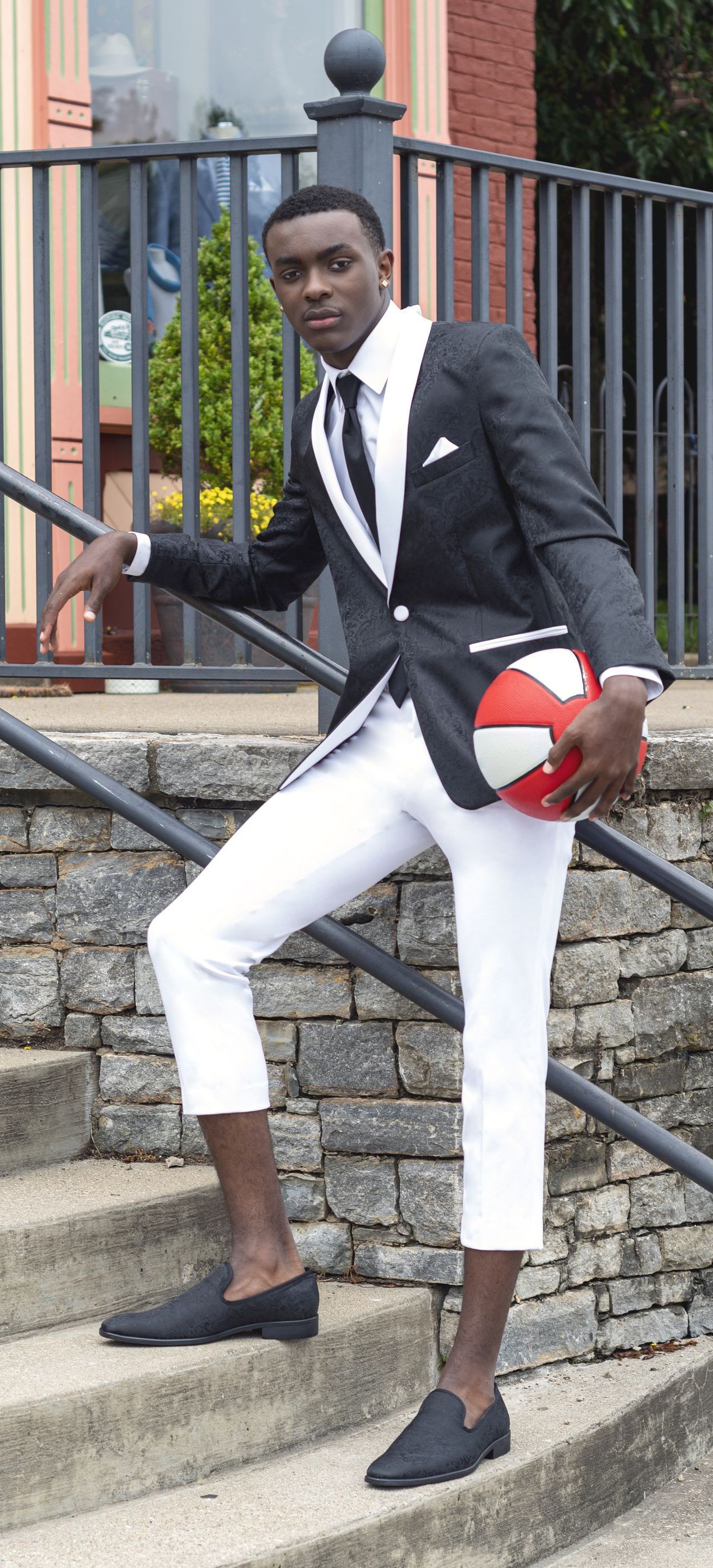A man in a suit and white pants is holding a red ball