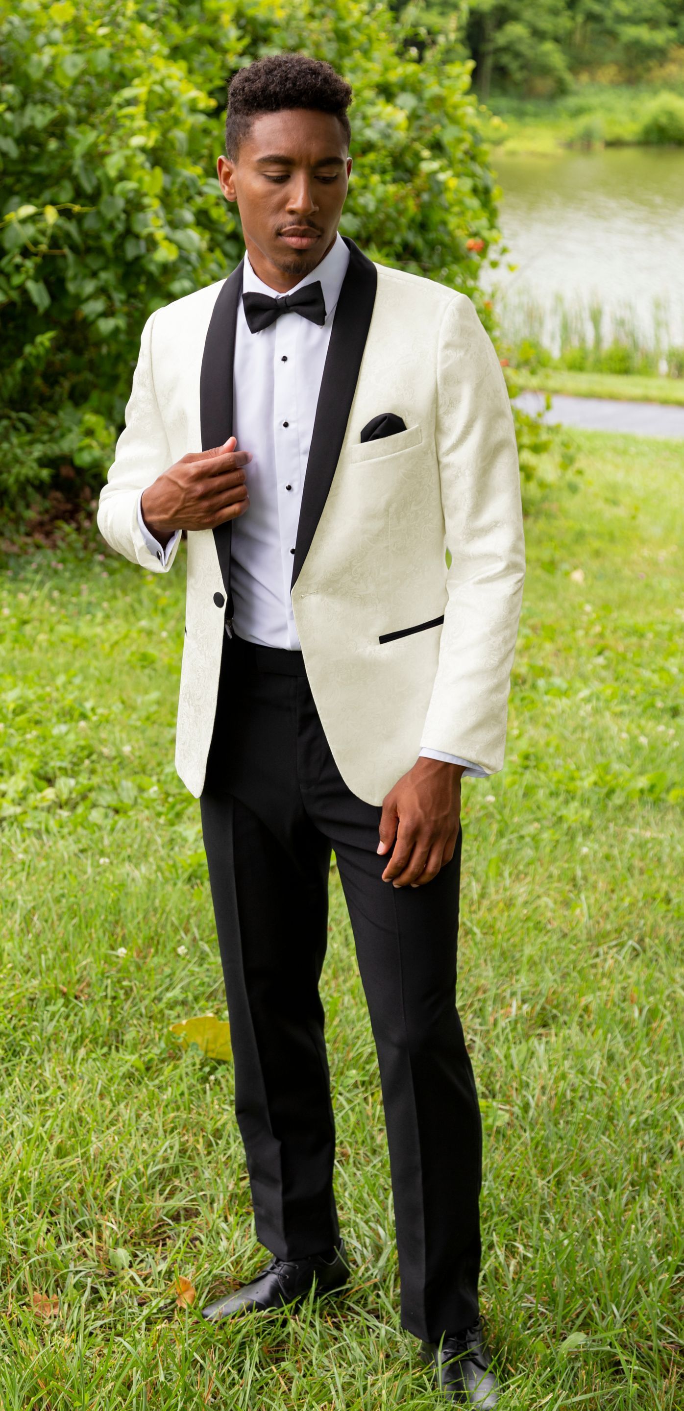 A man in a white tuxedo and black pants is standing in the grass.
