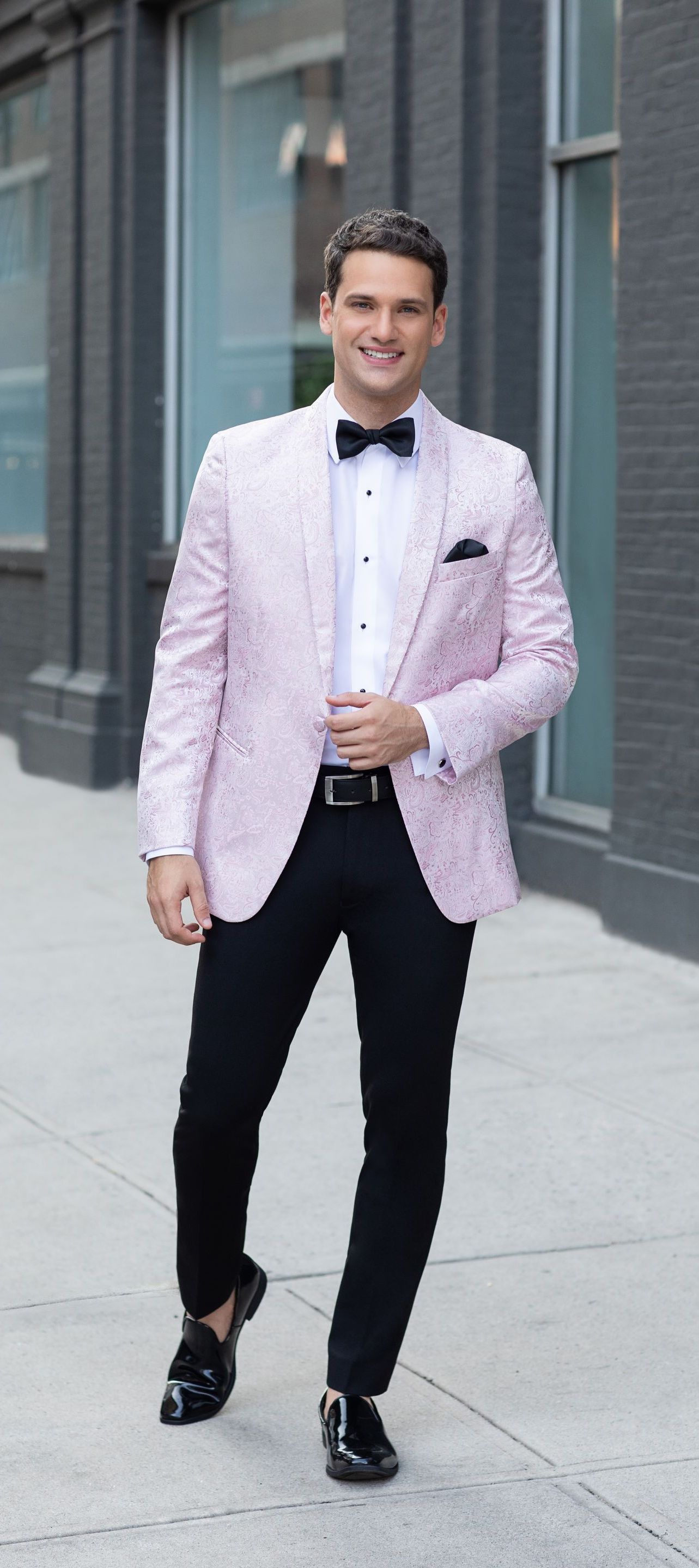 A man wearing a pink tuxedo jacket and black pants is walking down a sidewalk.