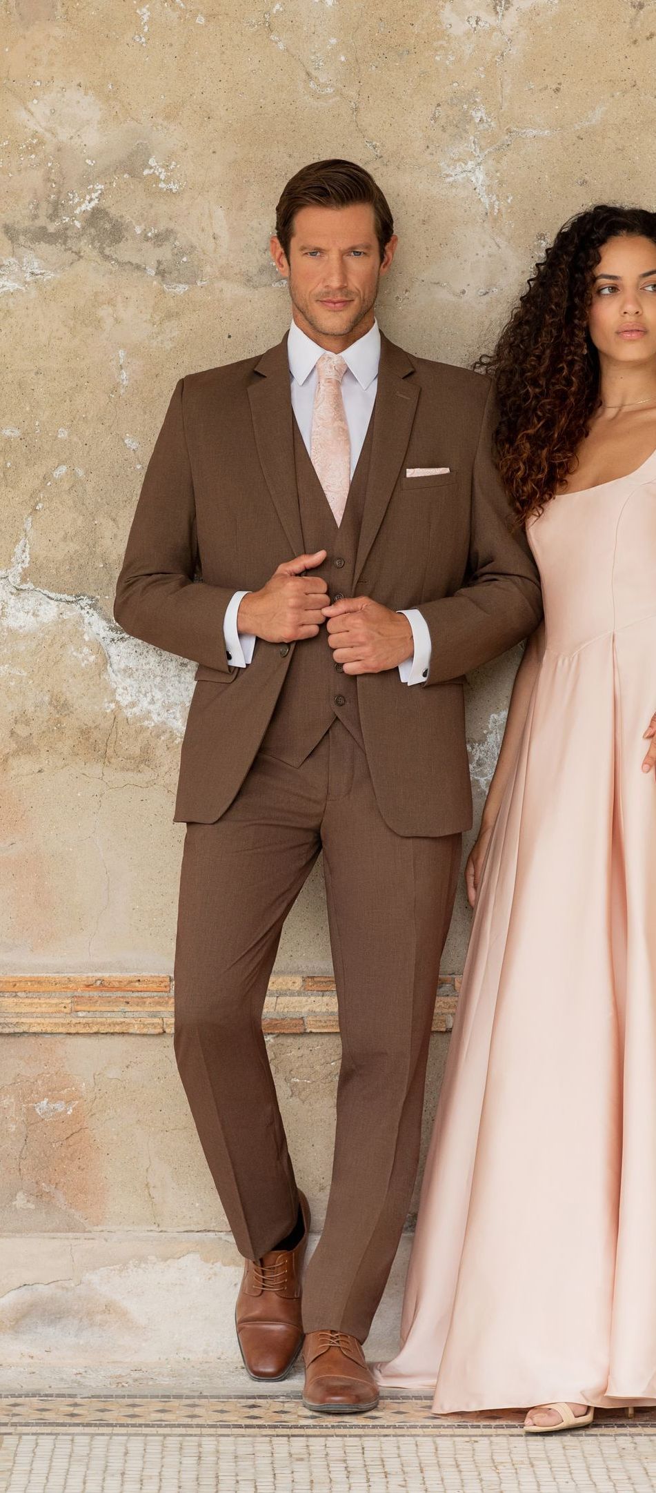 A man in a brown suit is standing next to a woman in a pink dress.