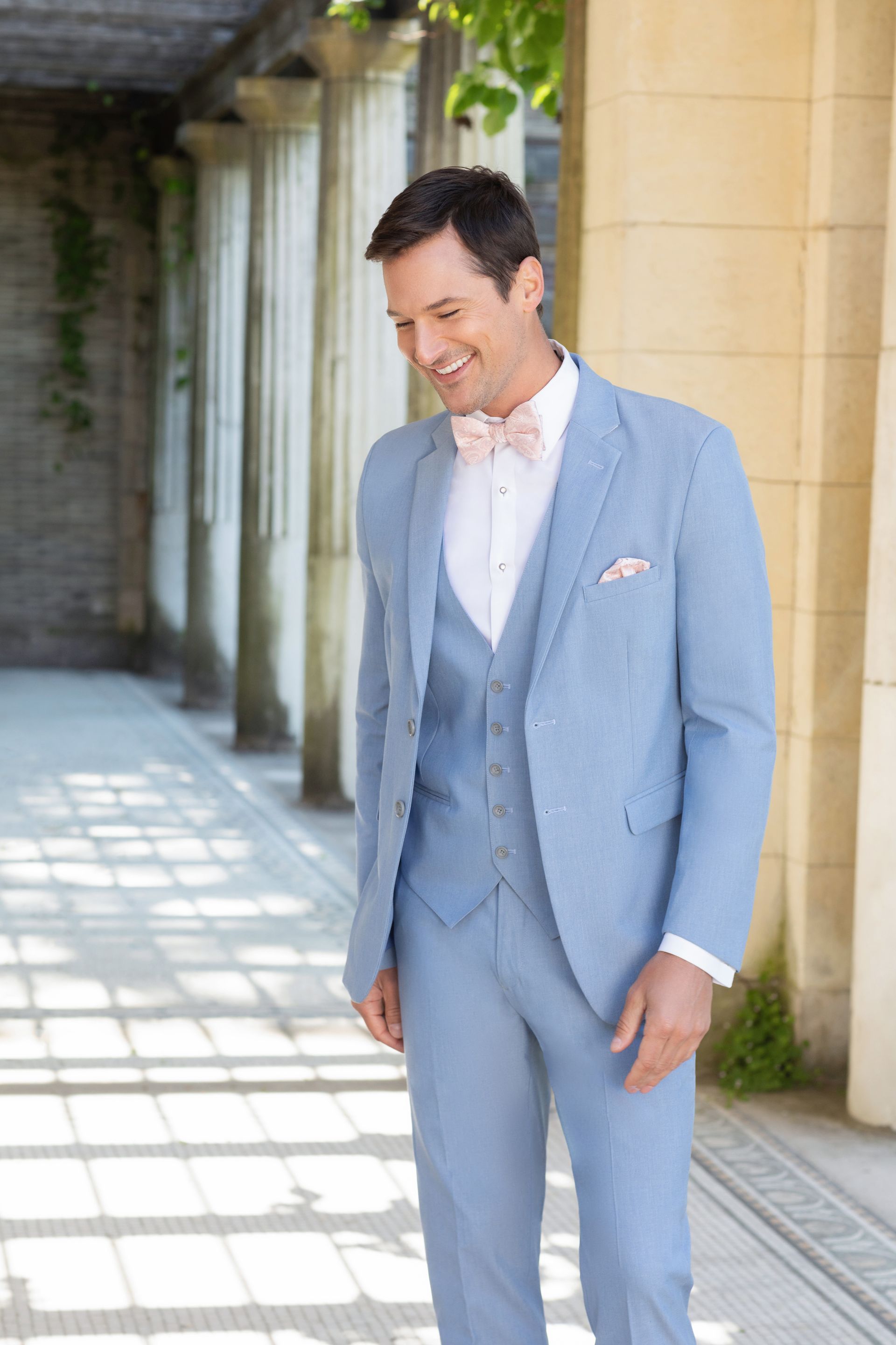 A man in a light blue suit and bow tie is standing in a hallway.