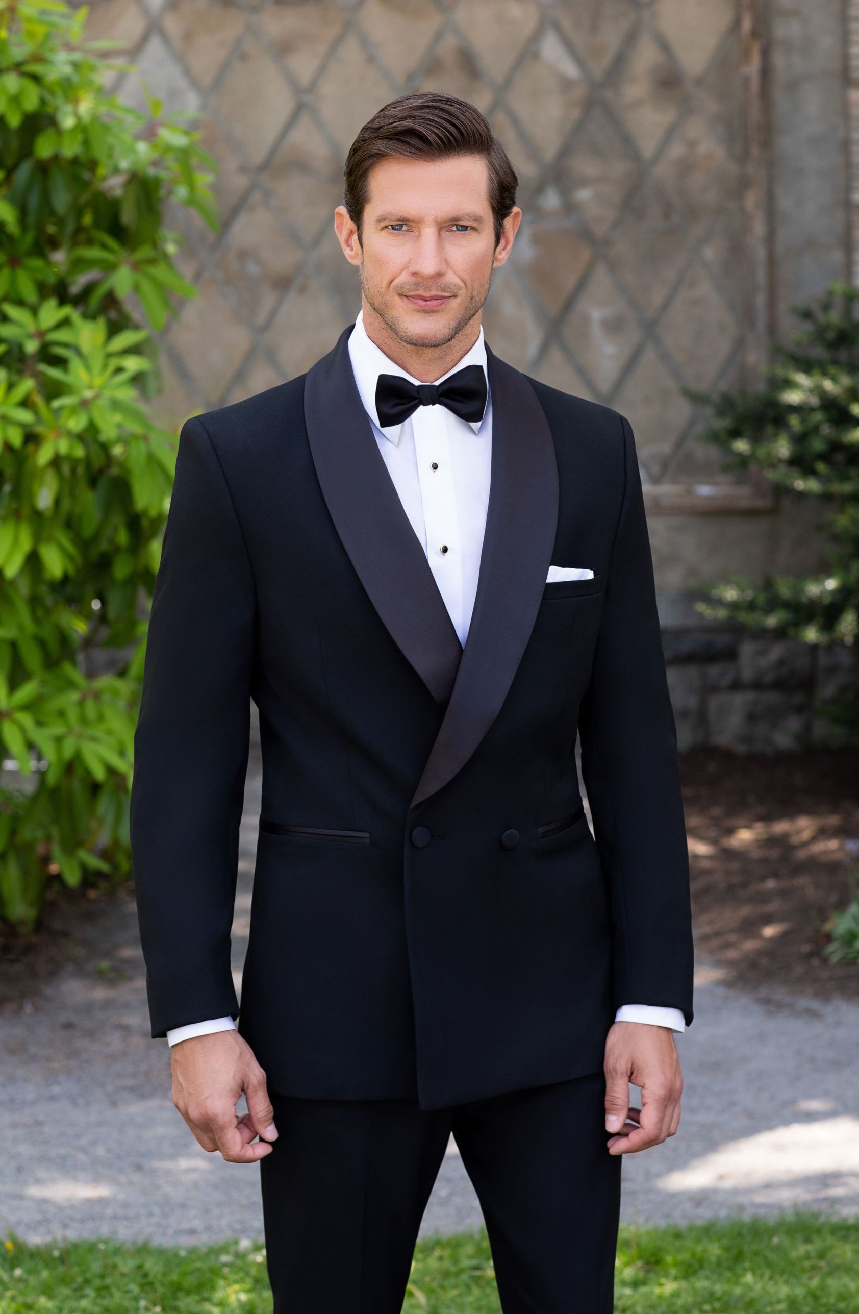 A man in a tuxedo and bow tie is standing in the grass.