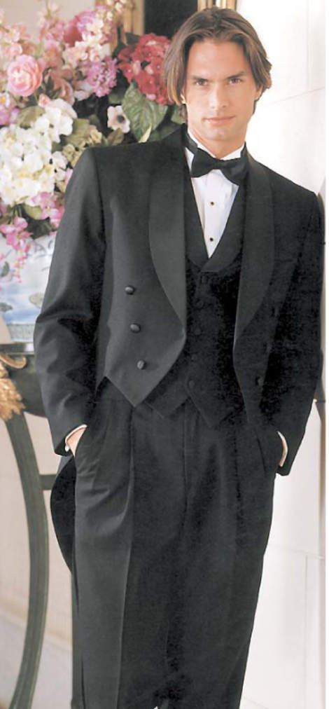 A man in a tuxedo and bow tie is standing in front of a vase of flowers.