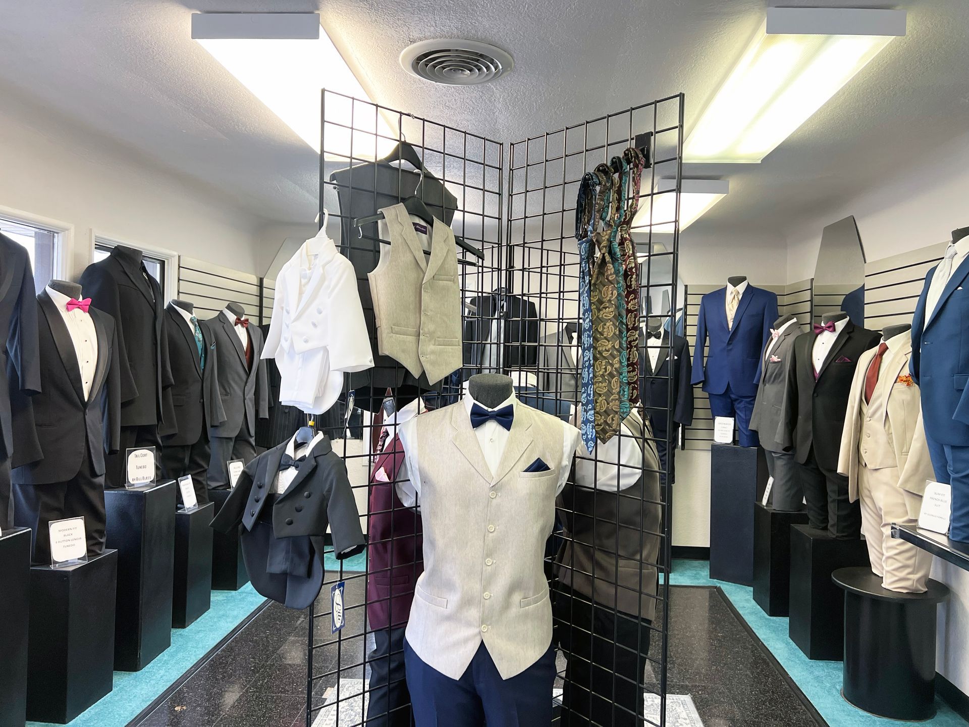 A store filled with lots of suits and tuxedos on mannequins.