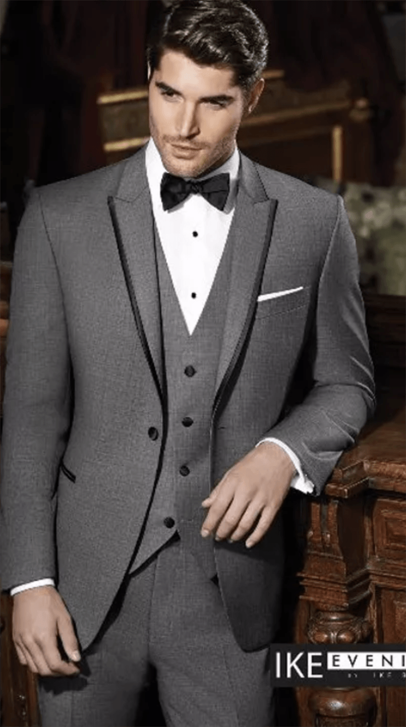 A man in a tuxedo and bow tie is standing next to a wooden railing.