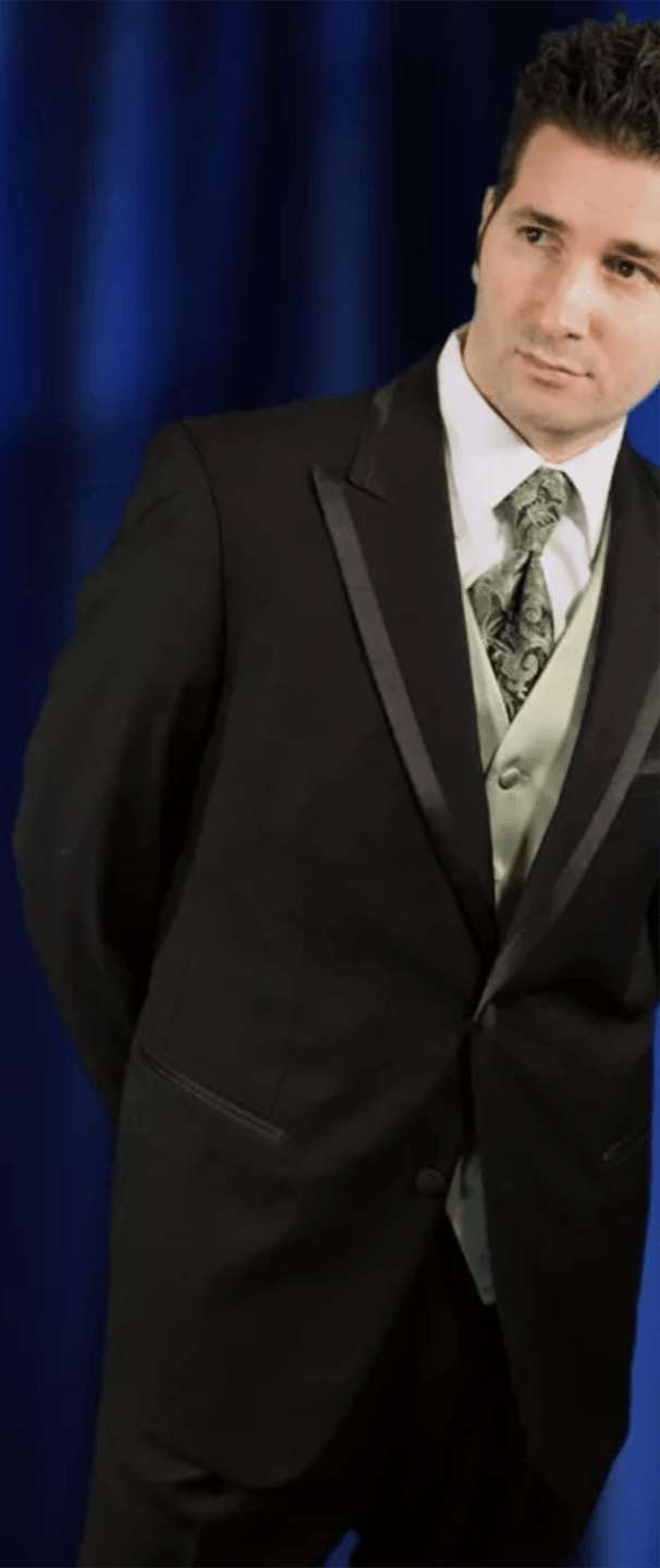A man in a tuxedo and tie is standing in front of a blue curtain