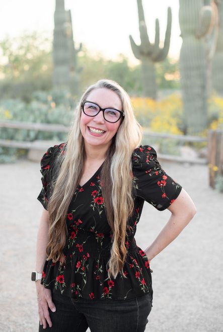 A woman wearing glasses and a black top is standing in front of a cactus.