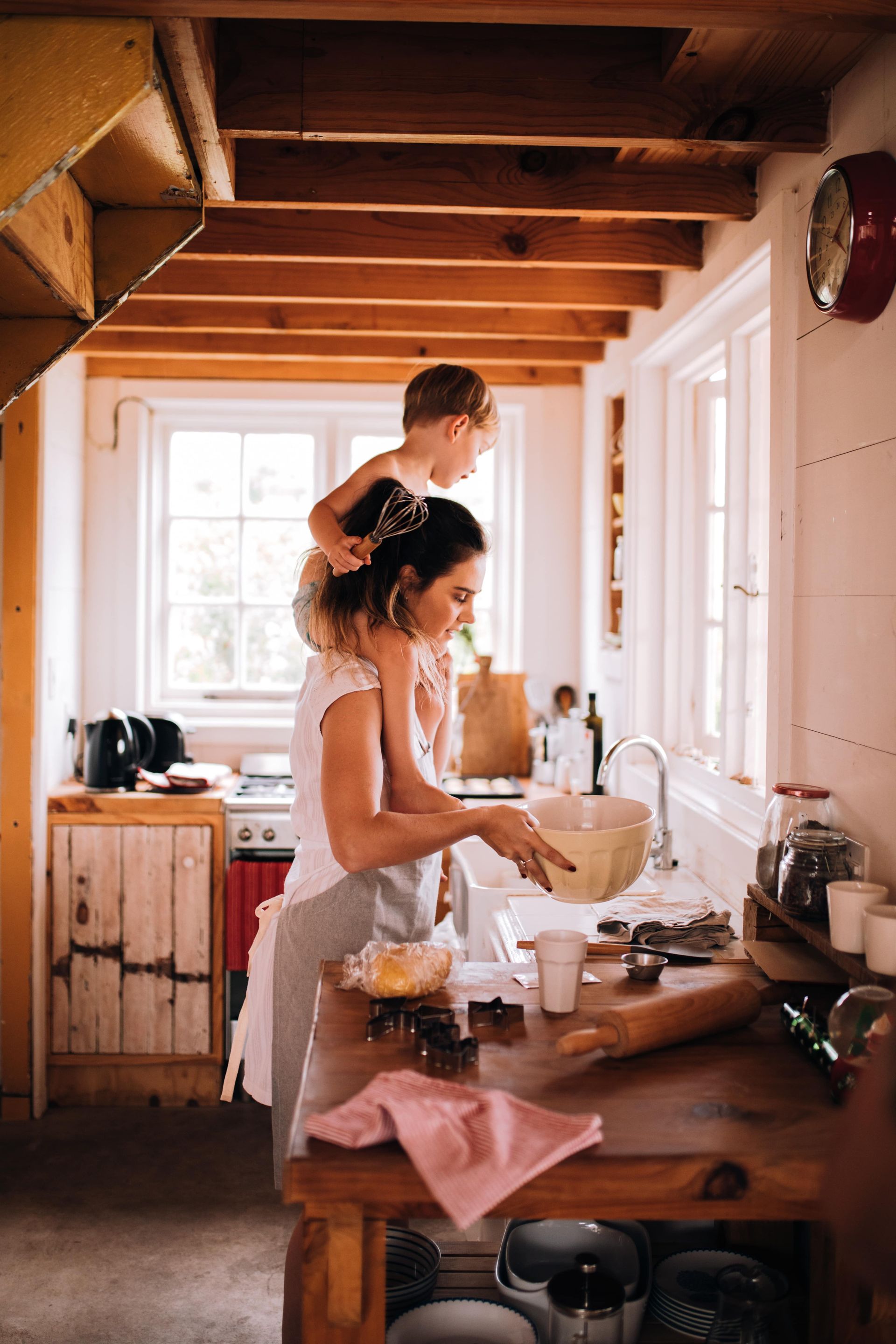 A woman is cooking in a kitchen with a child on her shoulders.