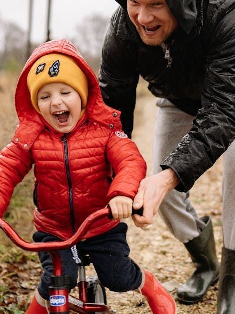 A man is helping a little boy ride a tricycle.