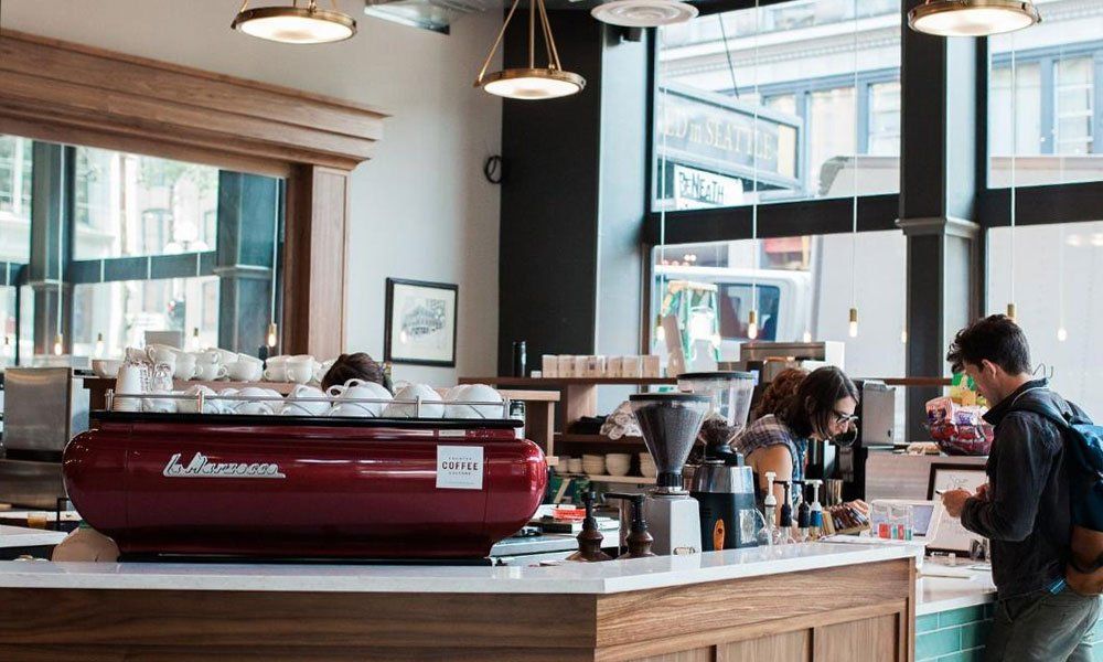 A man is standing at a counter in a coffee shop.