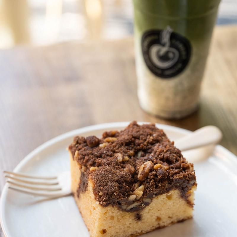 A piece of cake on a plate next to a cup of coffee
