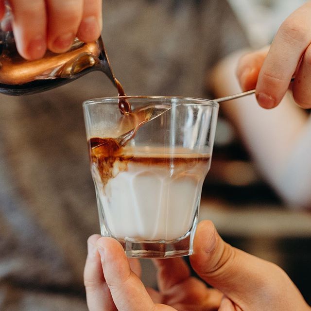 A person is pouring coffee into a glass with a spoon