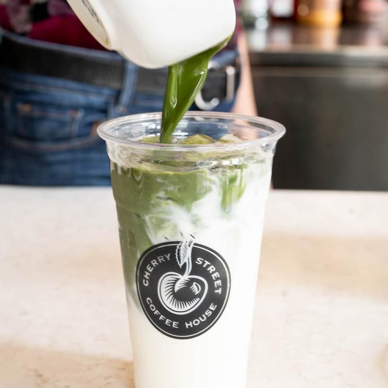 A person is pouring green tea into a cherry street coffee house cup.