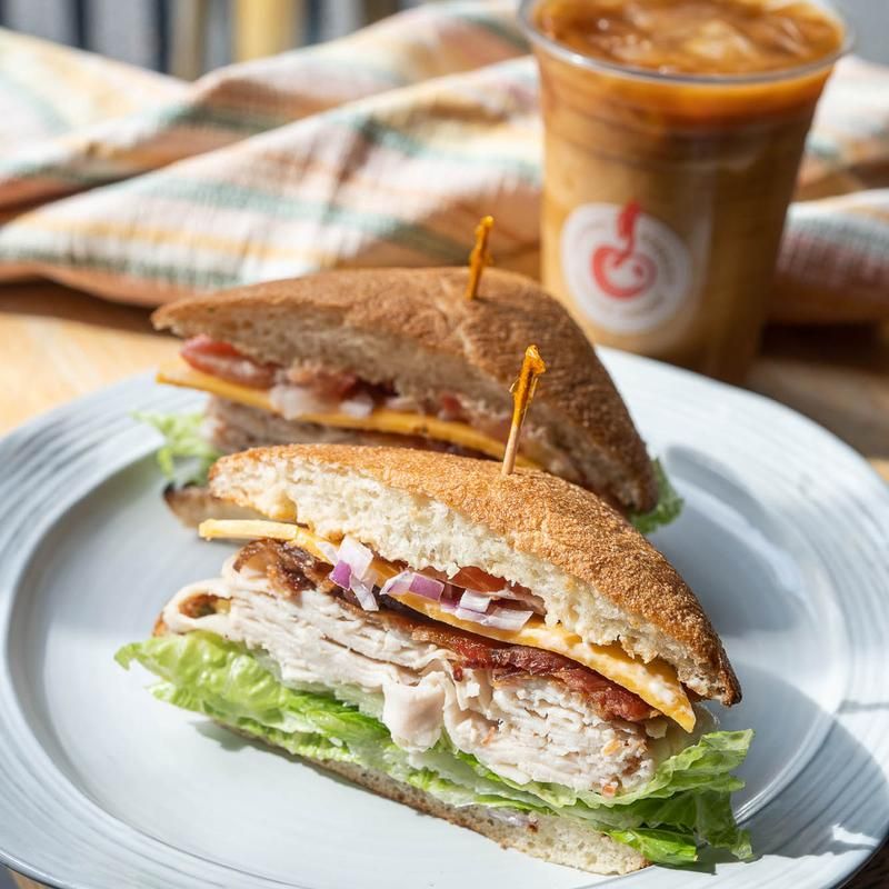 Two sandwiches are on a white plate next to a cup of coffee.