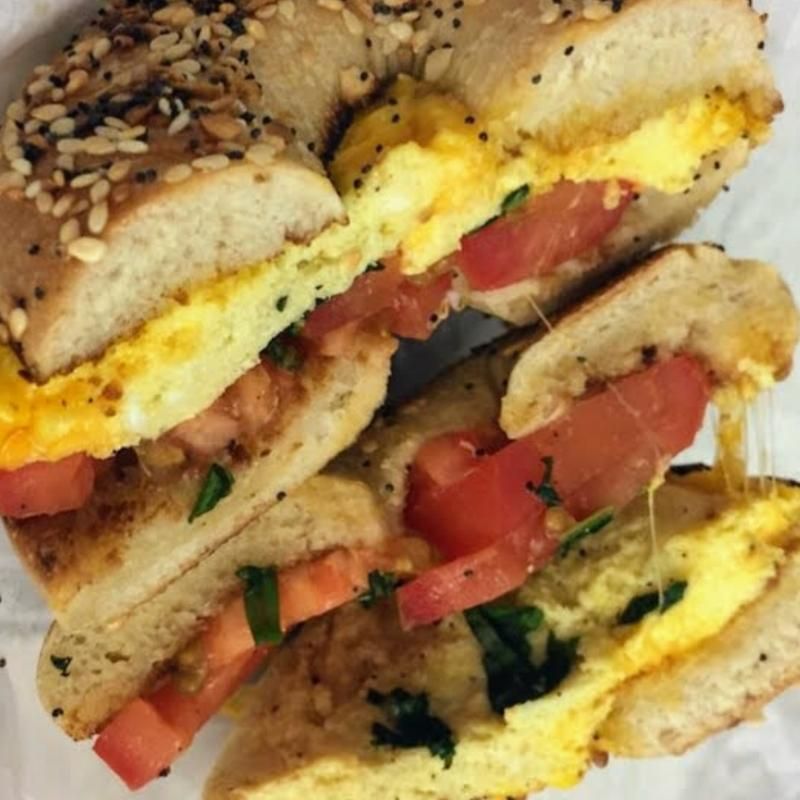 A close up of a bagel sandwich with eggs tomatoes and cheese