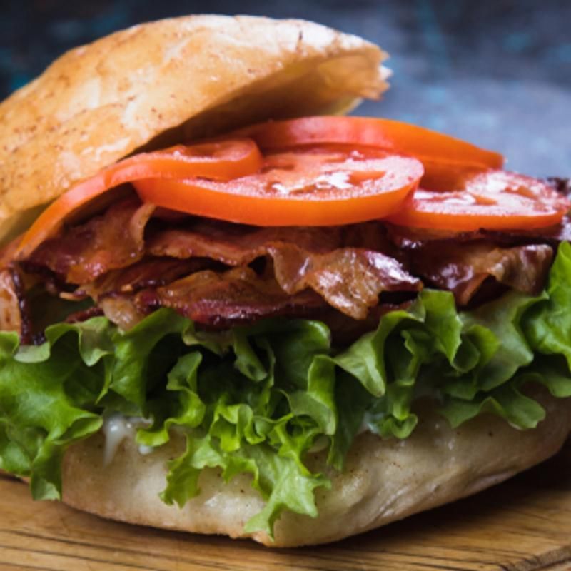 A close up of a sandwich with lettuce tomatoes and bacon on a wooden cutting board.