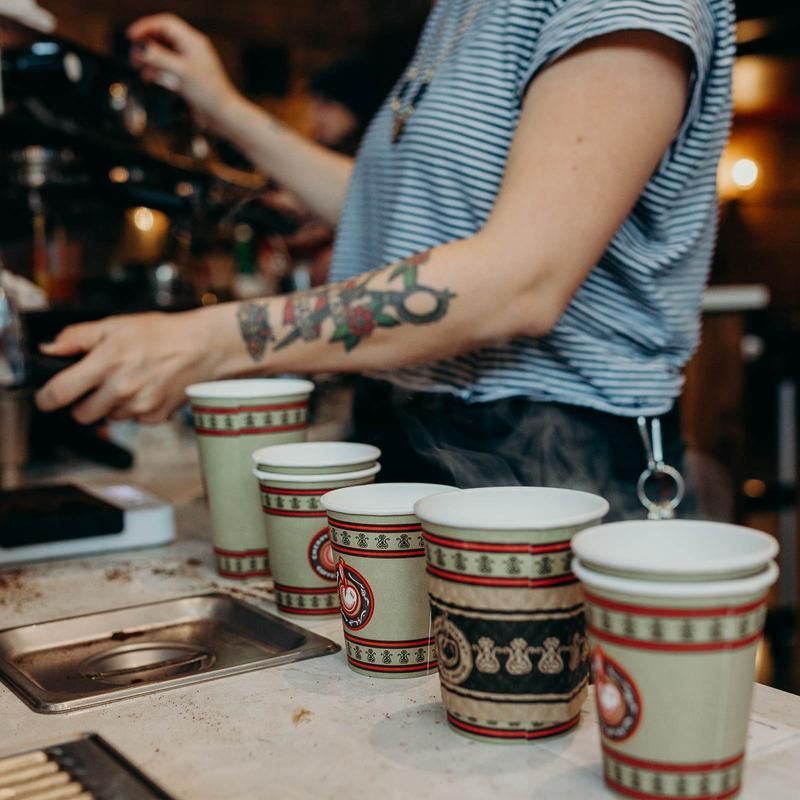 A woman with a tattoo on her arm is preparing coffee cups