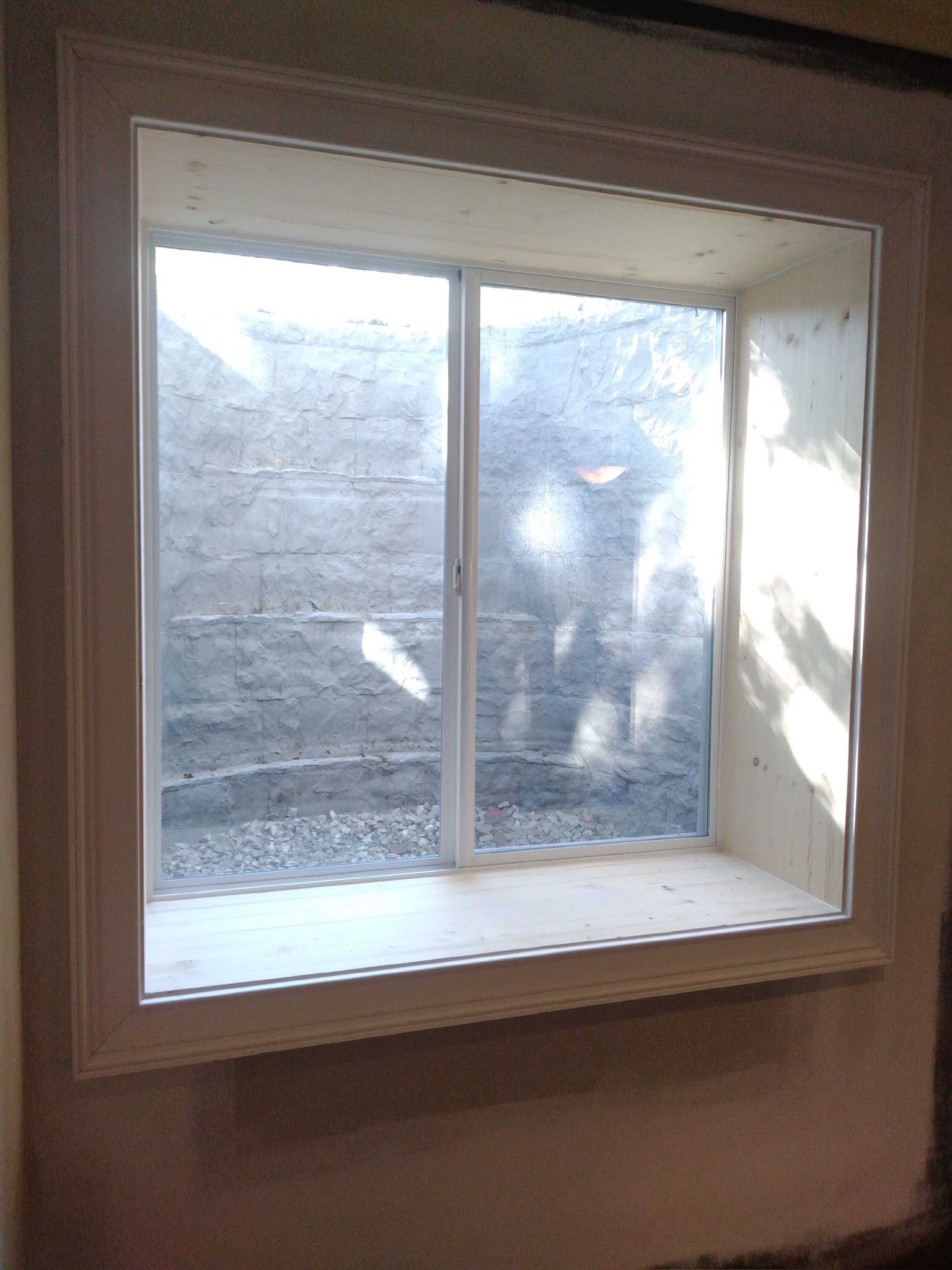 Basement window with wood trim and exposed concrete foundation behind the glass.