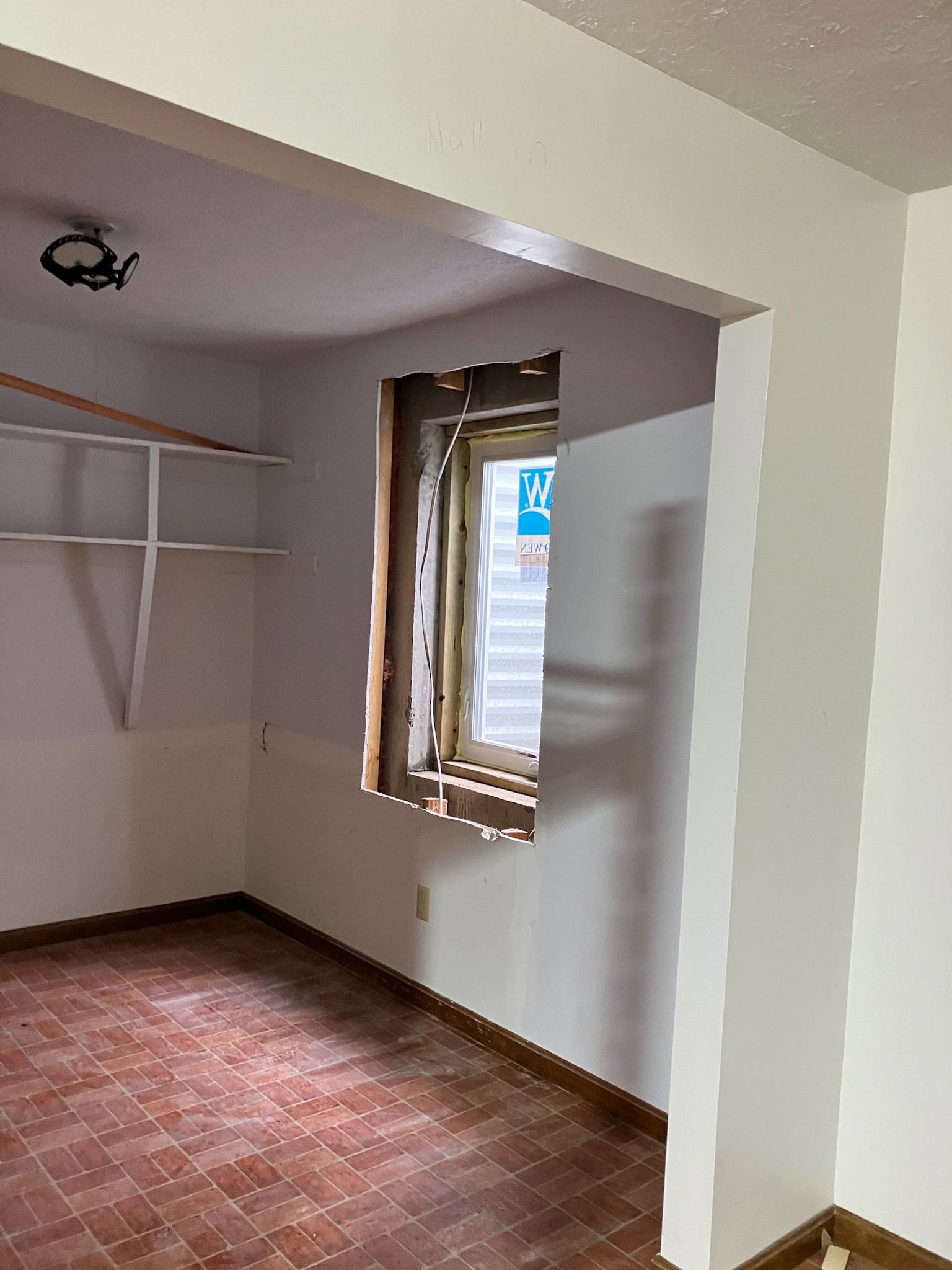Interior view of a room with an unfinished window and closet with shelves; brown floor and white walls.