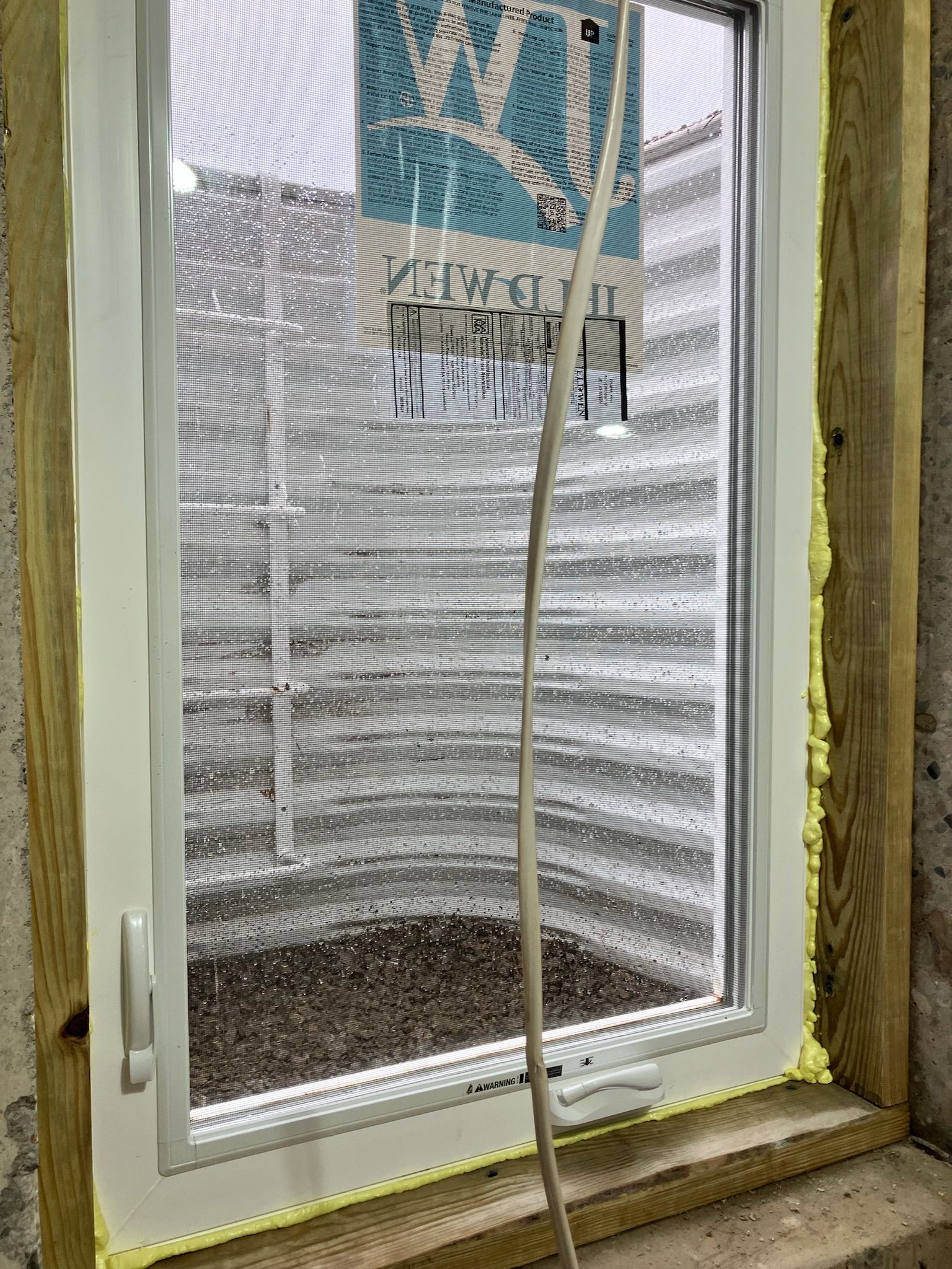 White window frame with a screen, set in a wooden frame with expanding foam insulation.